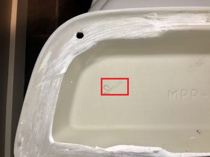 Inside of a toilet tank lid showing where the manufacture date is stamped.