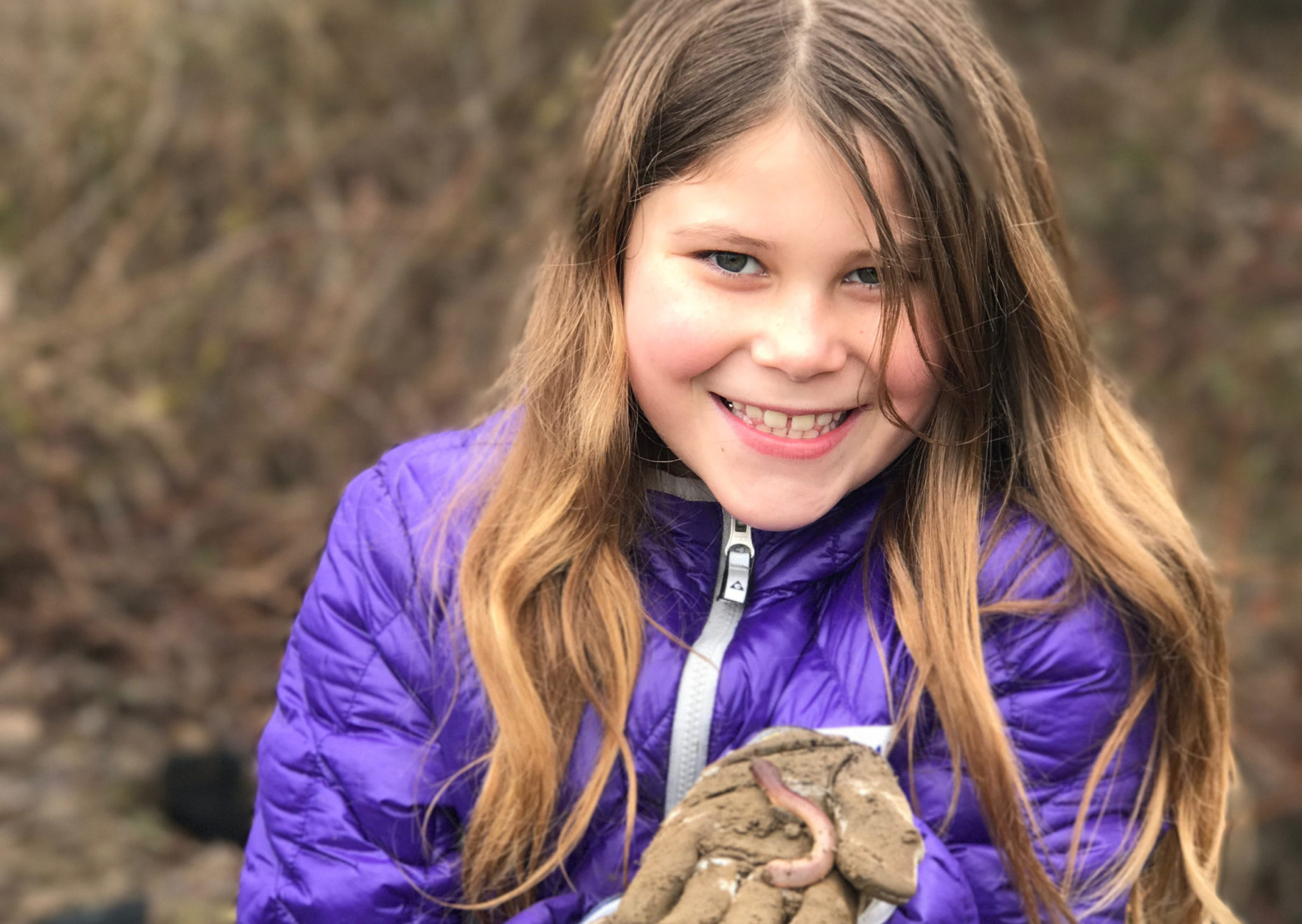 Young girl smiling while holding a worm outside