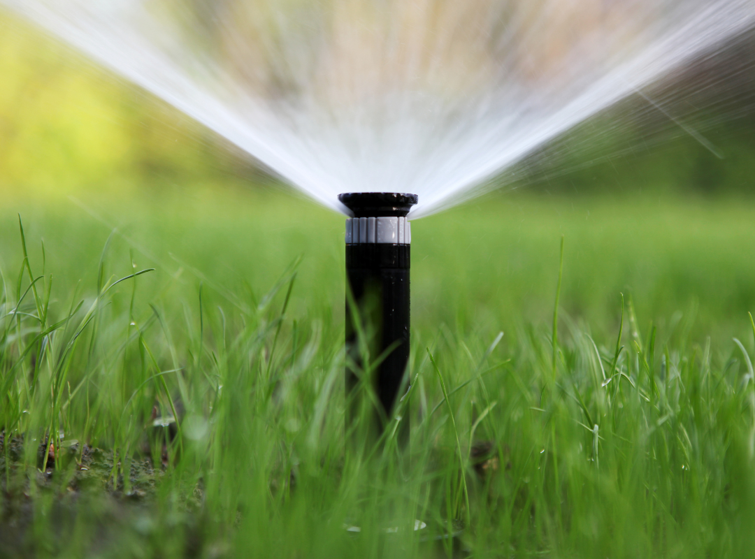 Shows a sprinkler head spraying water in a wide, flat, fan-shaped stream. 
