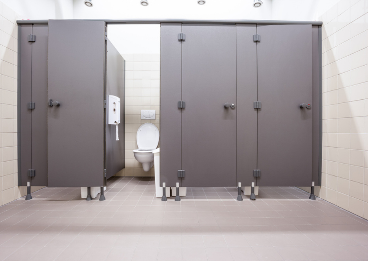 A row of bathroom stalls in a business, one door is open and you can see a white toilet.