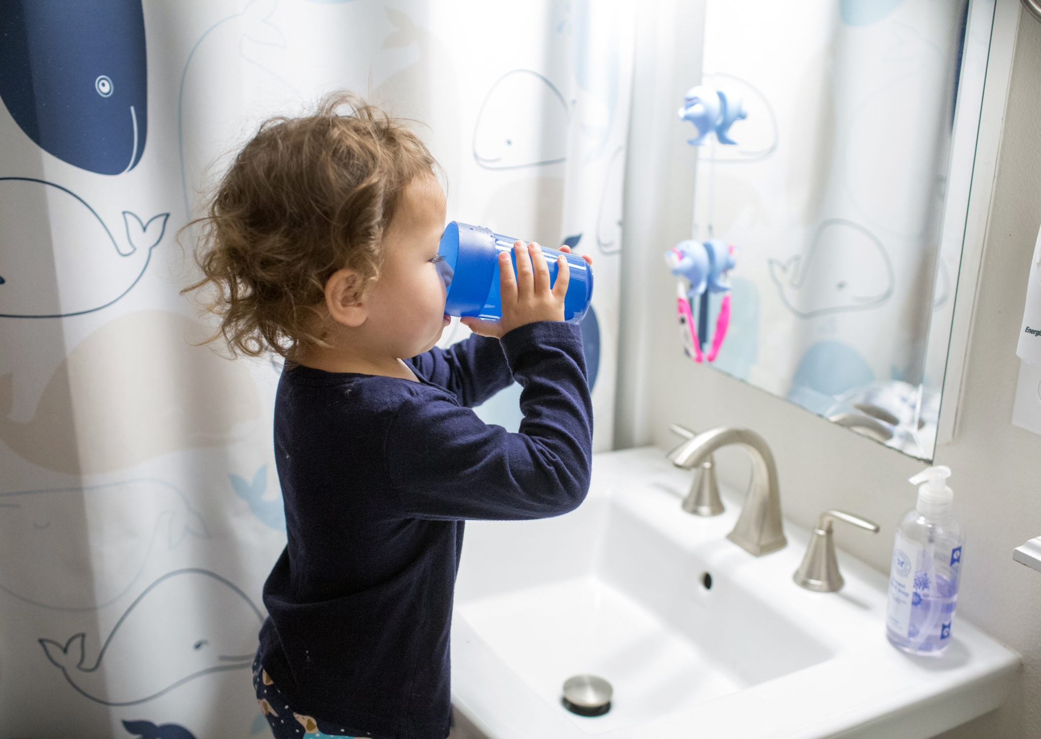 Young child standing at the bathroom sink taking a drink of water