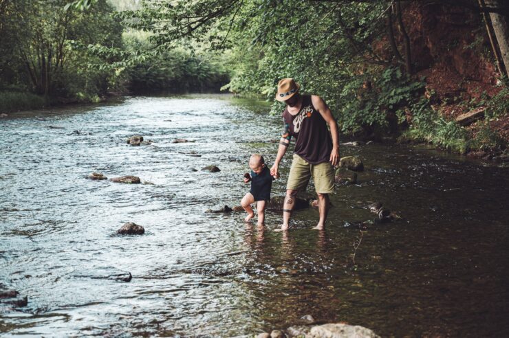 Father and young son holding hands as they walk across the river.