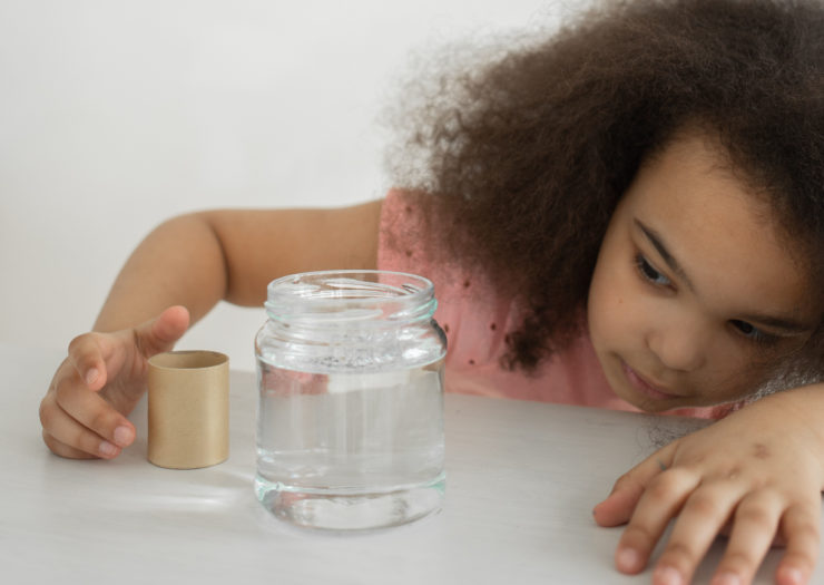 Young black girl leans over to get a better look at a jar of water